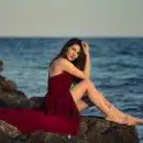 woman in red dress sitting on rock near sea during daytime