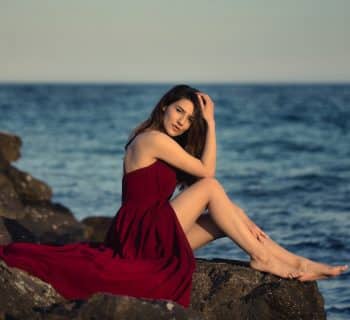 woman in red dress sitting on rock near sea during daytime