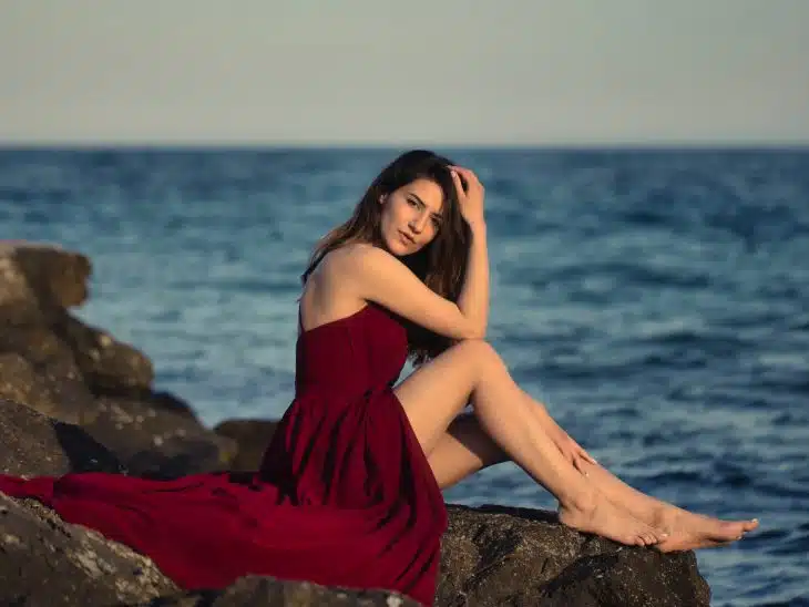 woman in red dress sitting on rock near sea during daytime