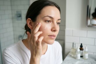 Jeune femme appliquant un sérum visage sur peau grasse dans une salle de bain minimaliste